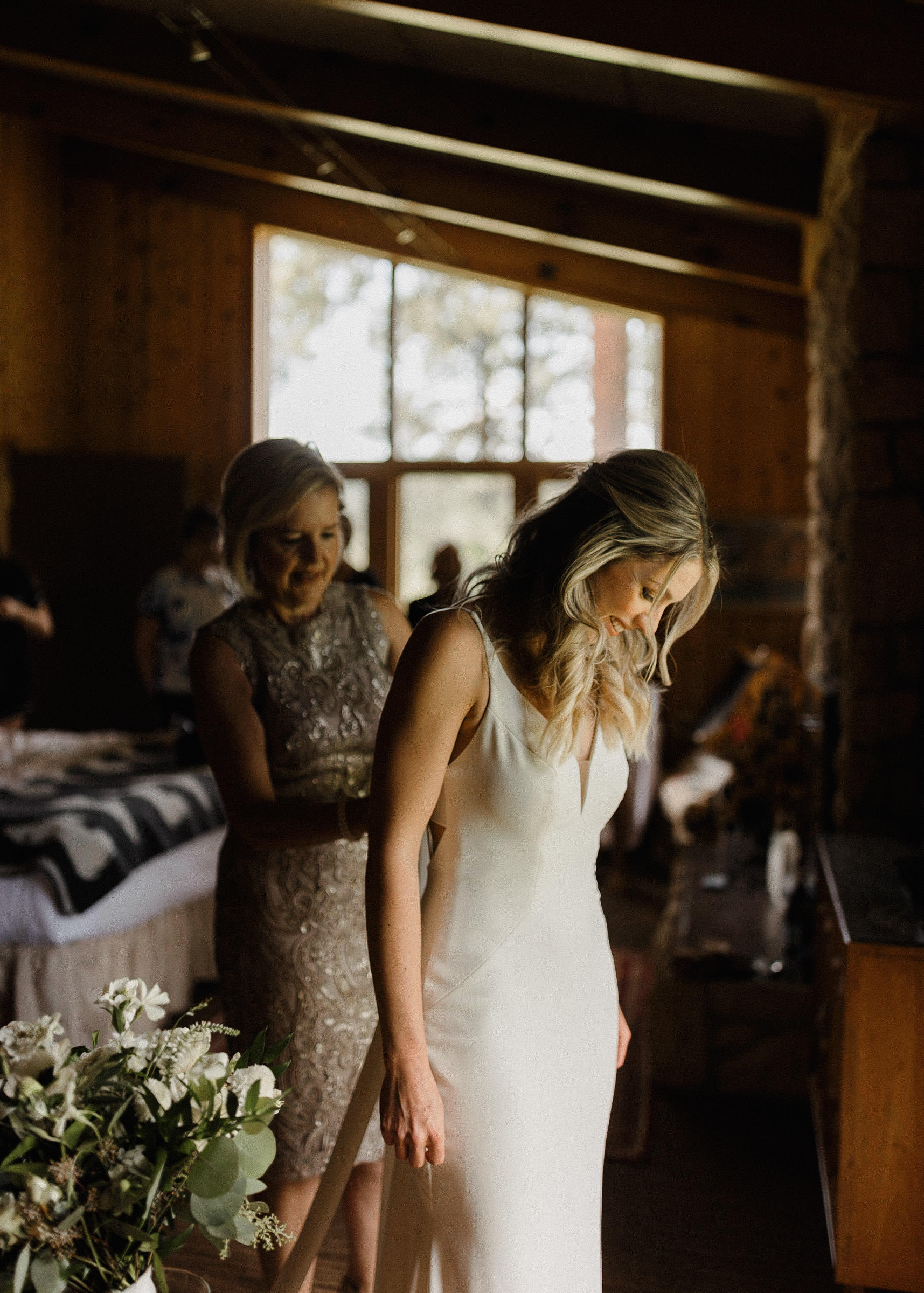 The mother of the bride buttons up the bride's dress