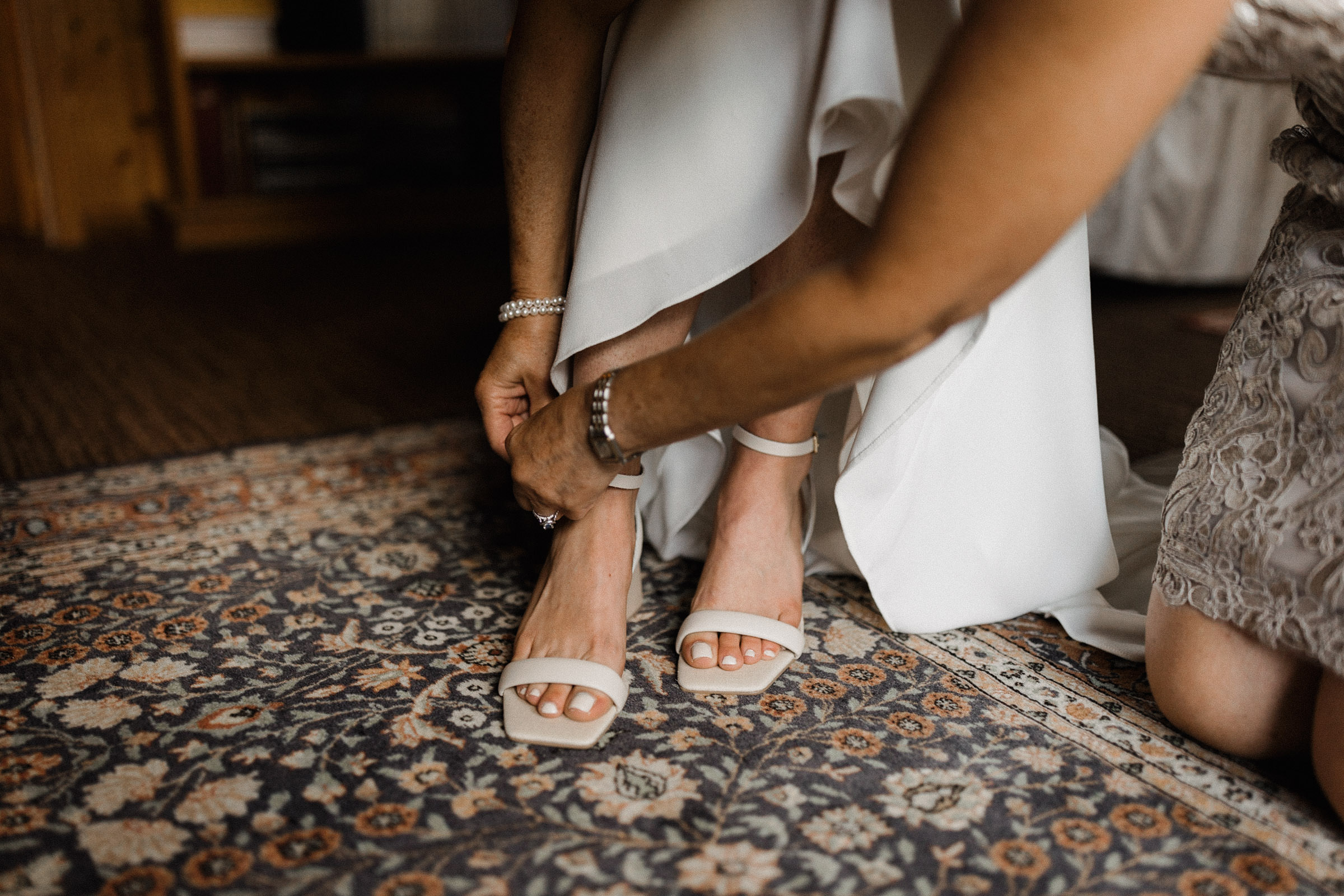 Bride's mother helps bride get her shoes on
