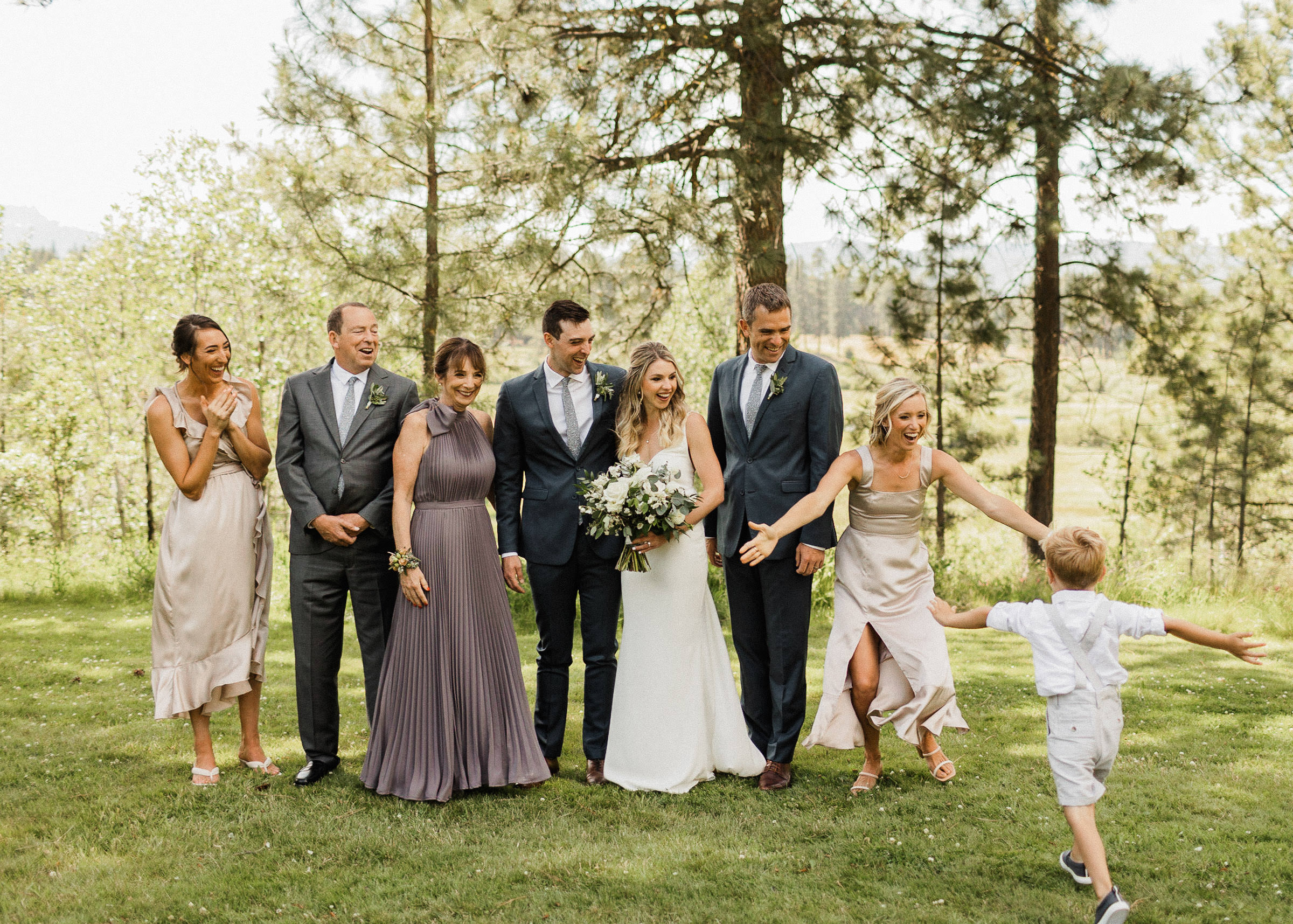 Family laughs and reacts warmly as young boy runs up to the groom's side of the family as they line up for a portrait