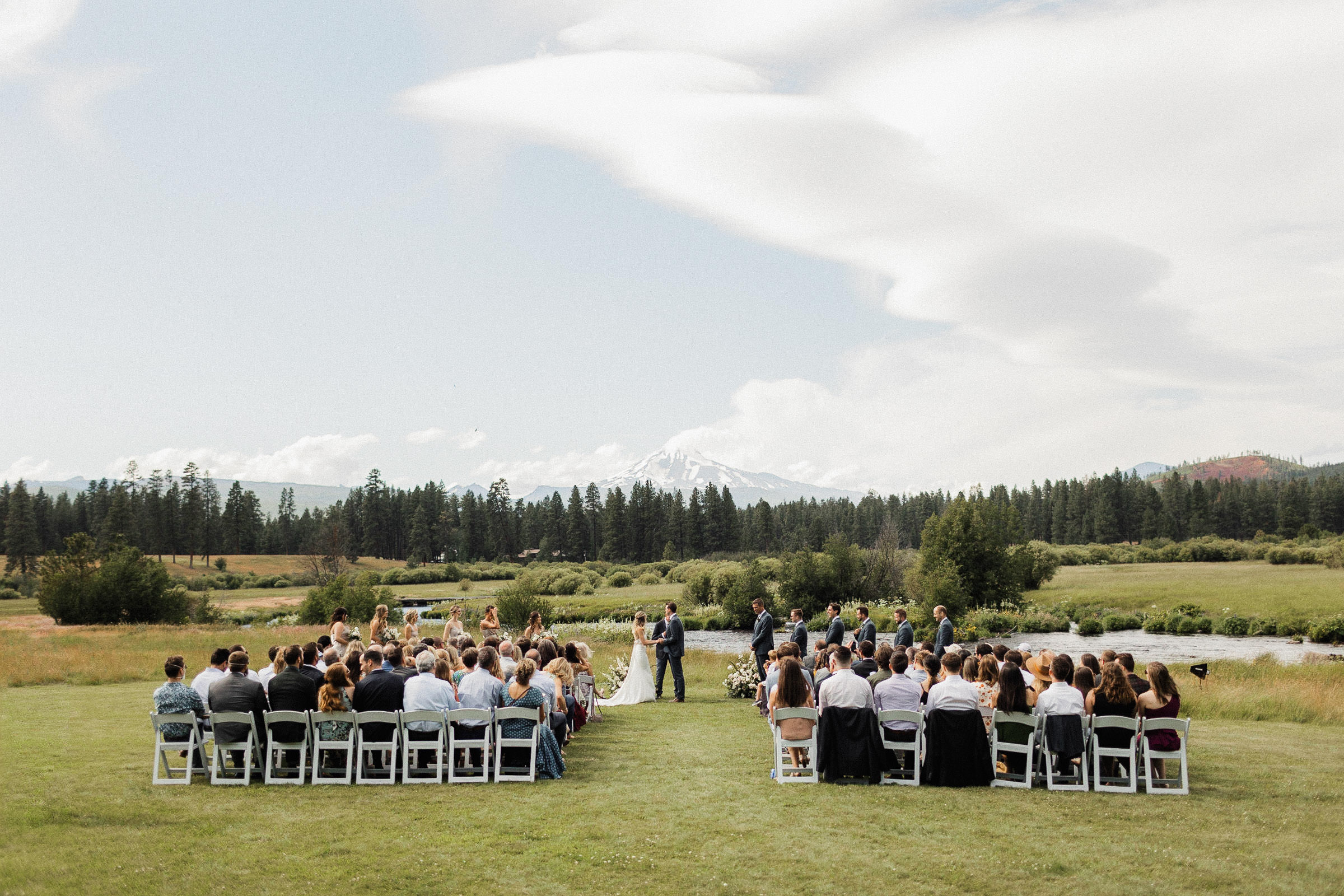 Wide view of the wedding ceremony in a field next the Metolius River, with Mt. Jefferson rising into the skyline