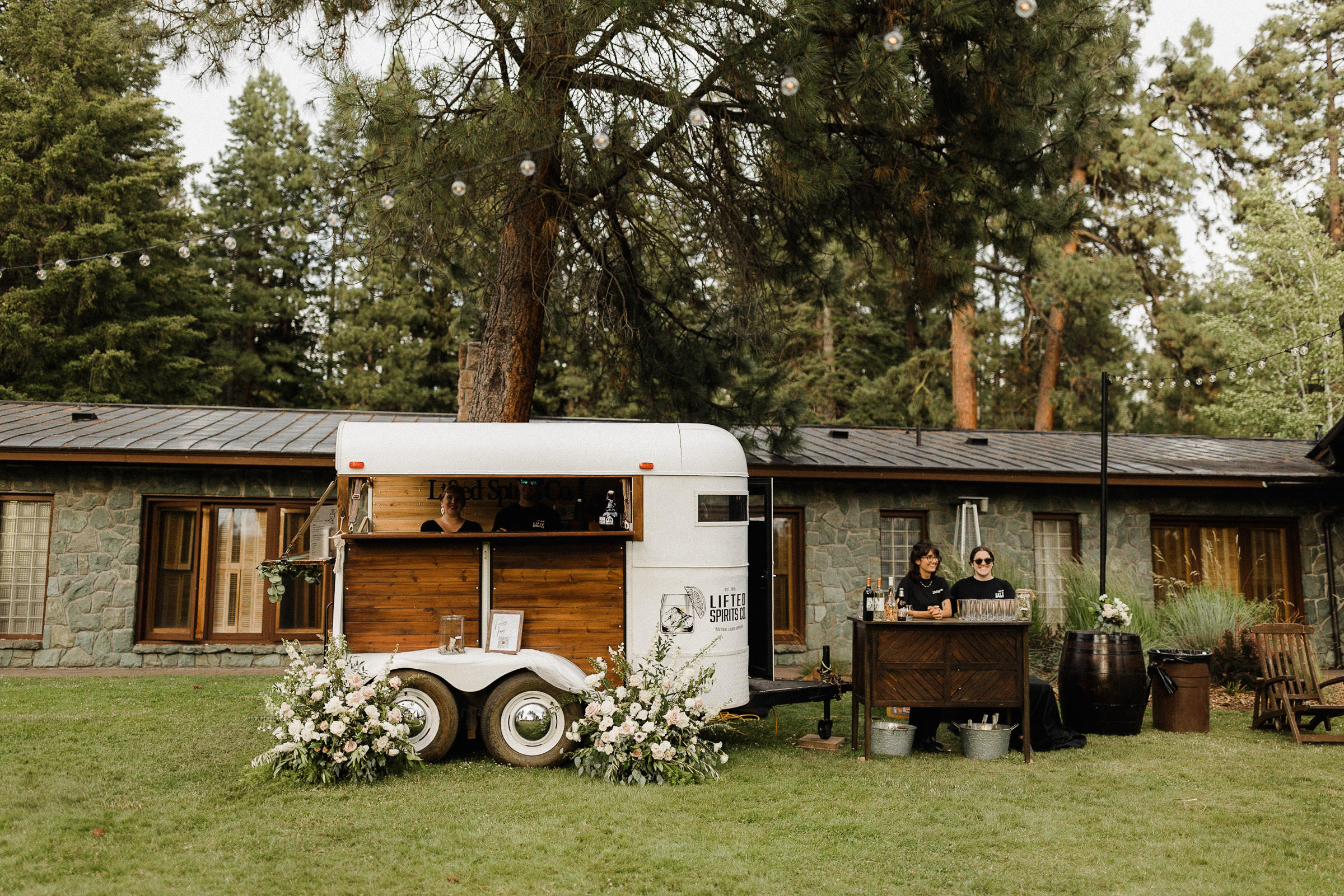 A mobile bar with florals is set up on the lawn outside House on the Metolius