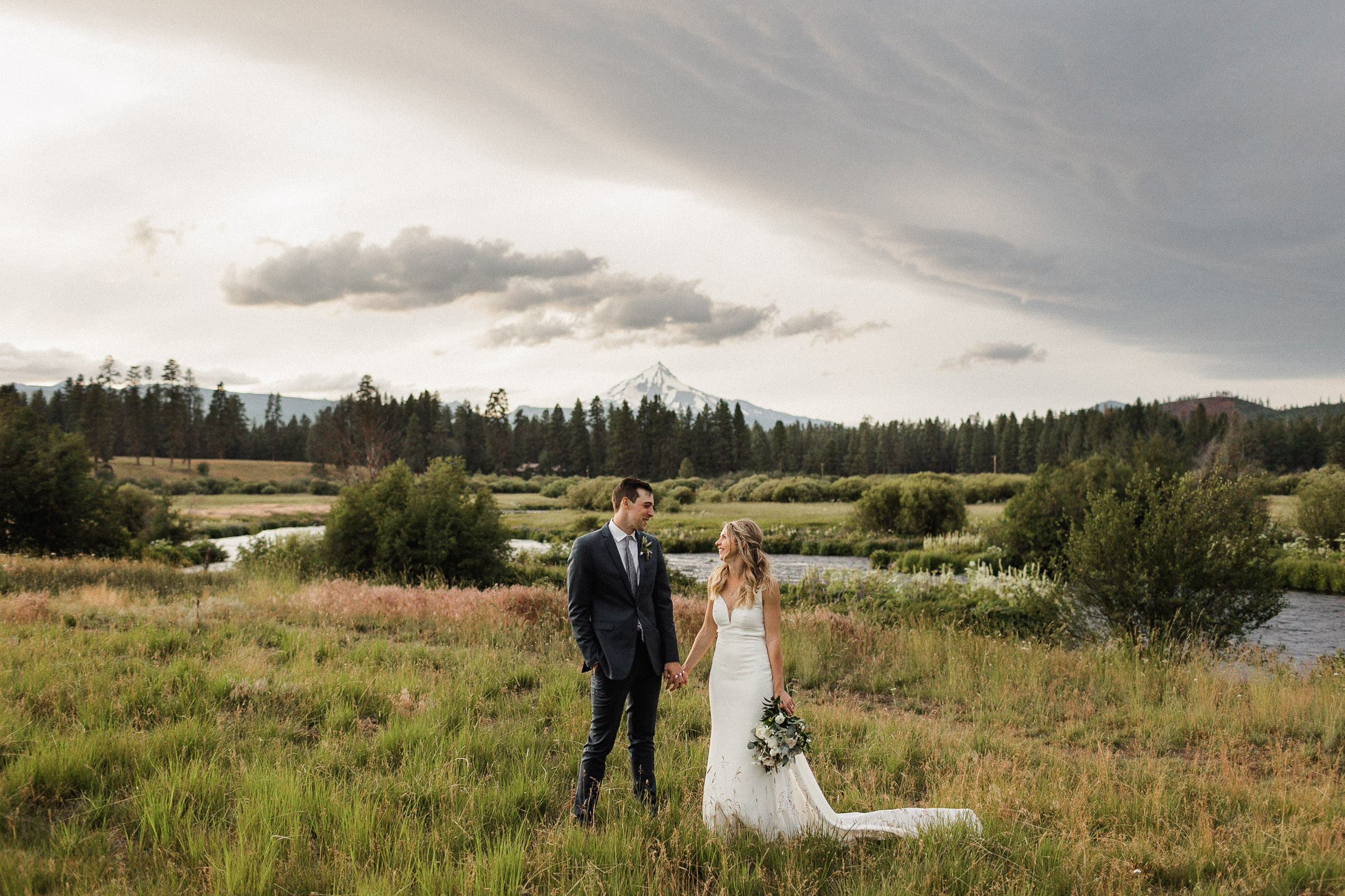Bride and groom hold hands, with a view of Mt. Jefferson