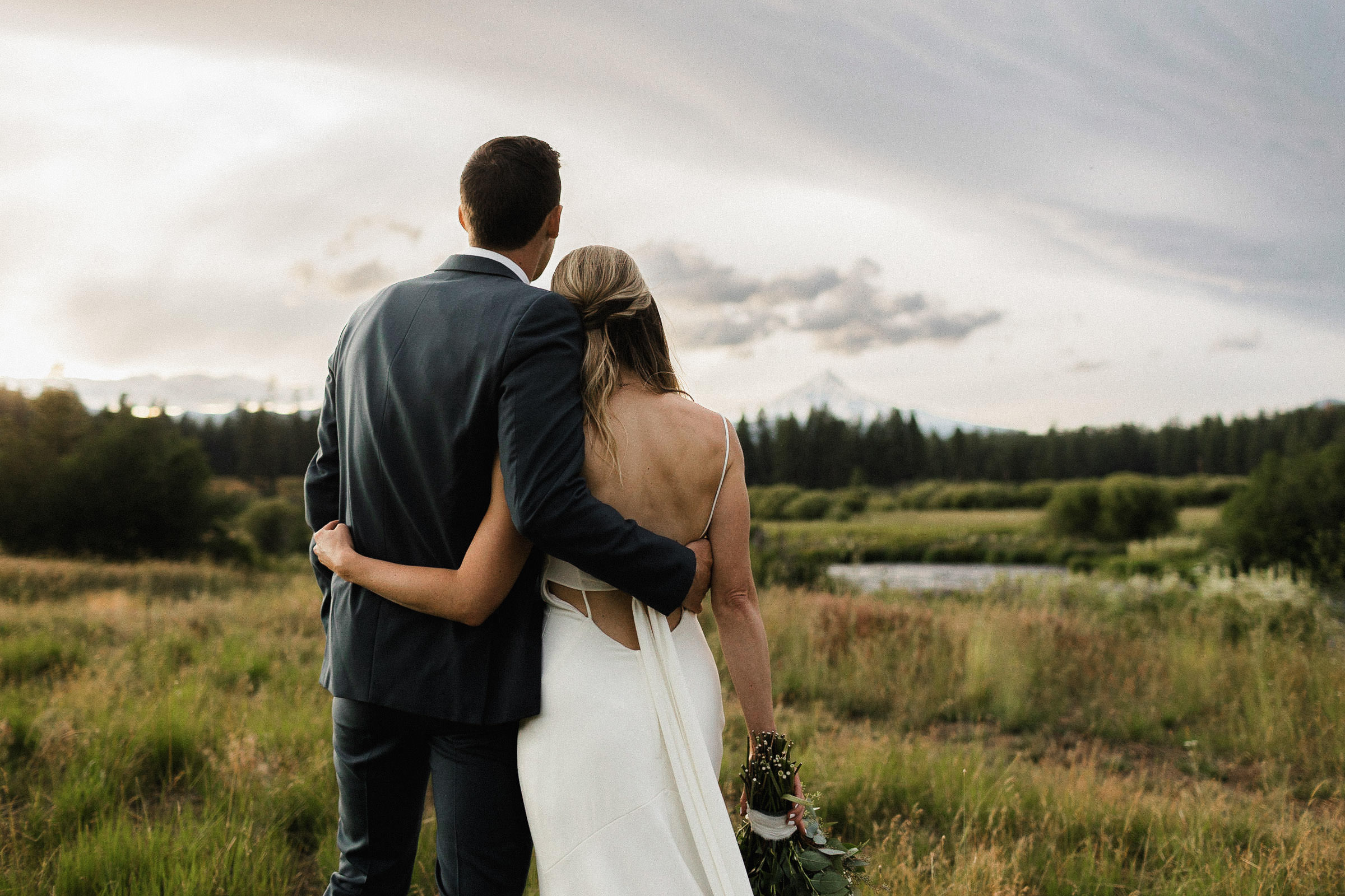 Bride and groom hold each other as they look at the mountain view